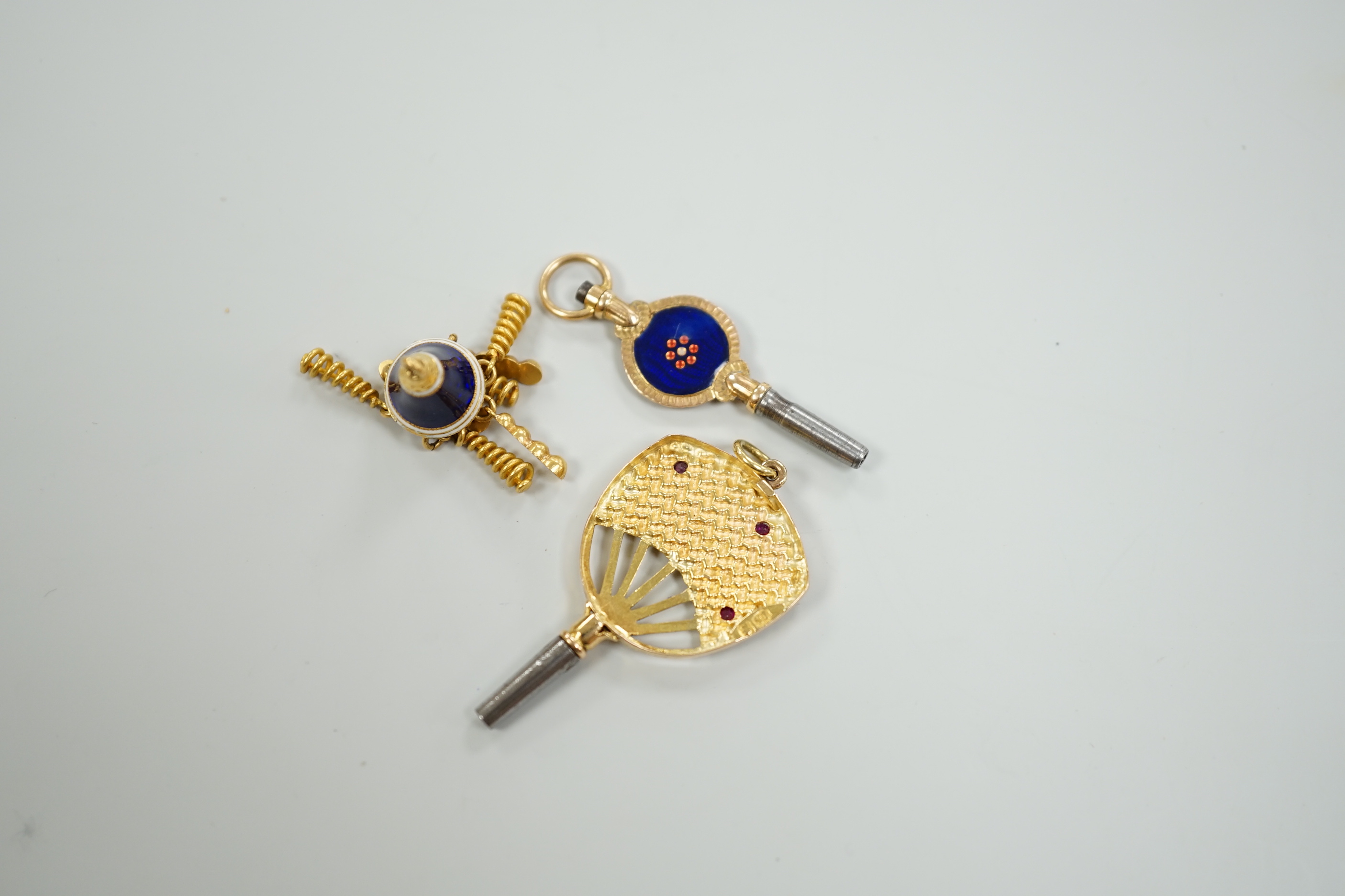 An early 20th century yellow metal (stamped 15), ruby and diamond set watch key, 39mm, together with a three colour enamelled watch key and an enamelled tassel charm.